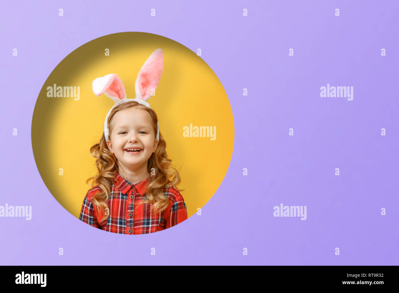 Ritratto di una incantevole piccola ragazza con orecchie di coniglietto. Felice Pasqua. Bambino in un foro rotondo in cerchio colorato di giallo e viola e sfondi Foto Stock