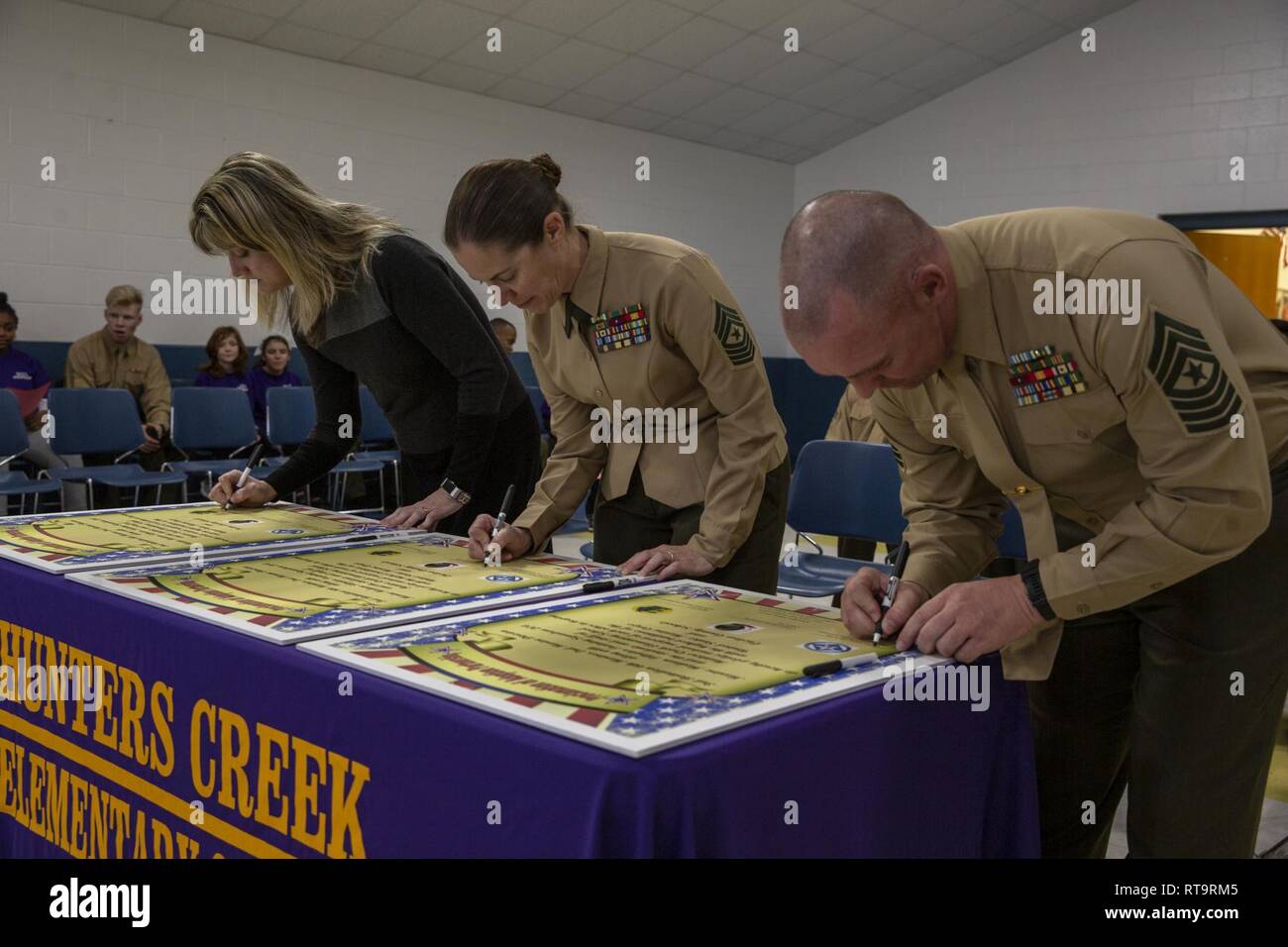 Stati Uniti Marine Corps Sgt. Il Mag. Jody Armentrout, battaglione sergente maggiore, 3° Battaglione. 6° Reggimento Marine (6Mar Reg), seconda divisione Marine, Sgt. Il Mag. Jennifer Armentrout, squadrone sergente maggiore, Marine medie Tiltrotor Training Squadron 204 (VMMT-204), Marine Aircraft Group 26, 2 aeromobili Marina Wing e Teah Bulris, principale di cacciatori Creek Scuola Elementare di firmare un annuncio di adozione del documento di partenariato durante il sesto Mar Reg e VMMT-204, adottare-a-scuola cerimonia al Hunters Creek Scuola Elementare di Jacksonville, N.C., 1 febbraio 2019. I partner del programma Marine Corps unità wit Foto Stock