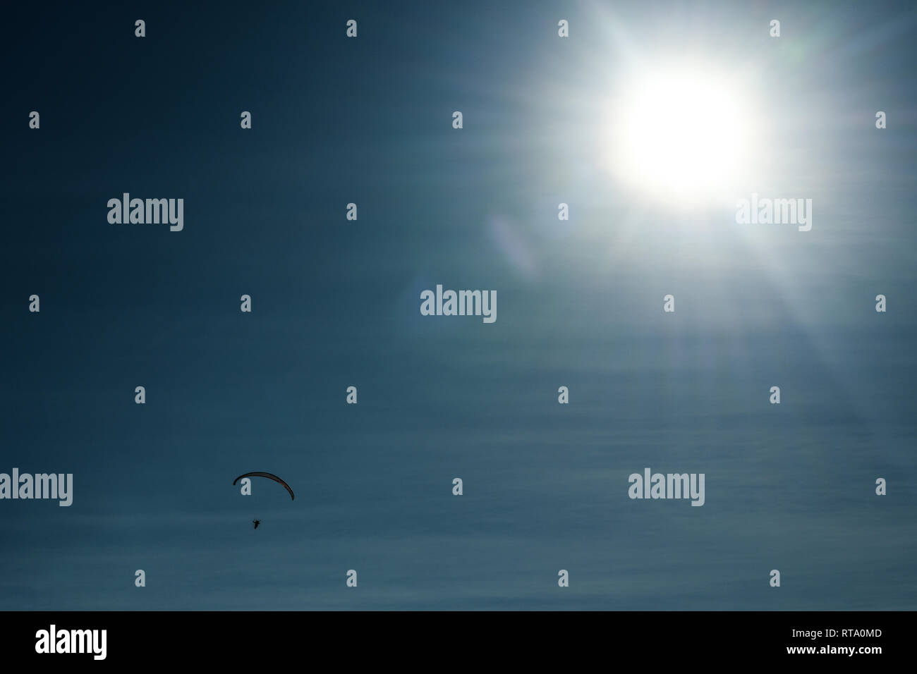 Silhouette di parachutist battenti sul paracadute nel bel cielo azzurro. Sun flares. Foto Stock