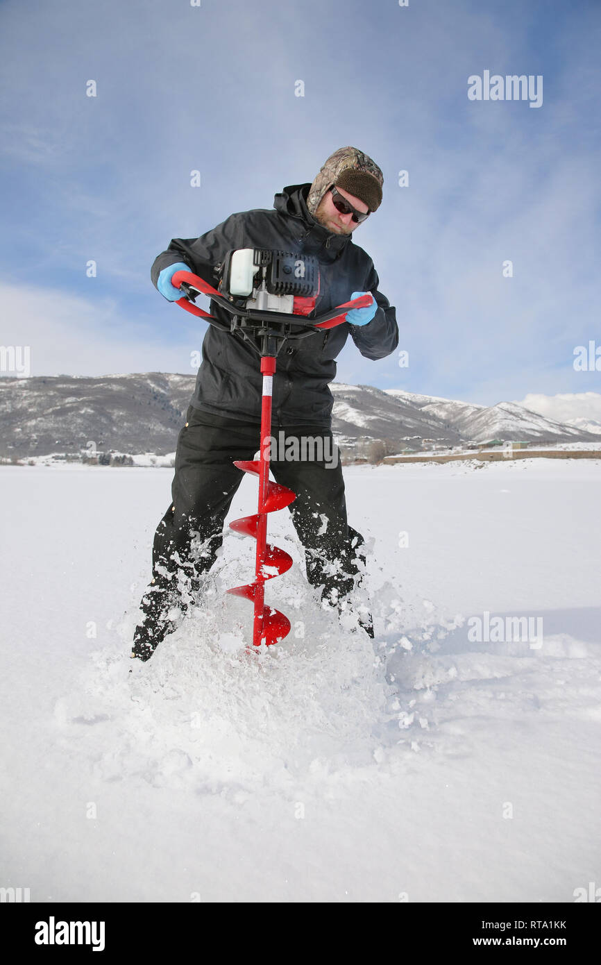 Adulto pescatore di ghiaccio di praticare un foro nel ghiaccio con un lago con una coclea di alimentazione Foto Stock