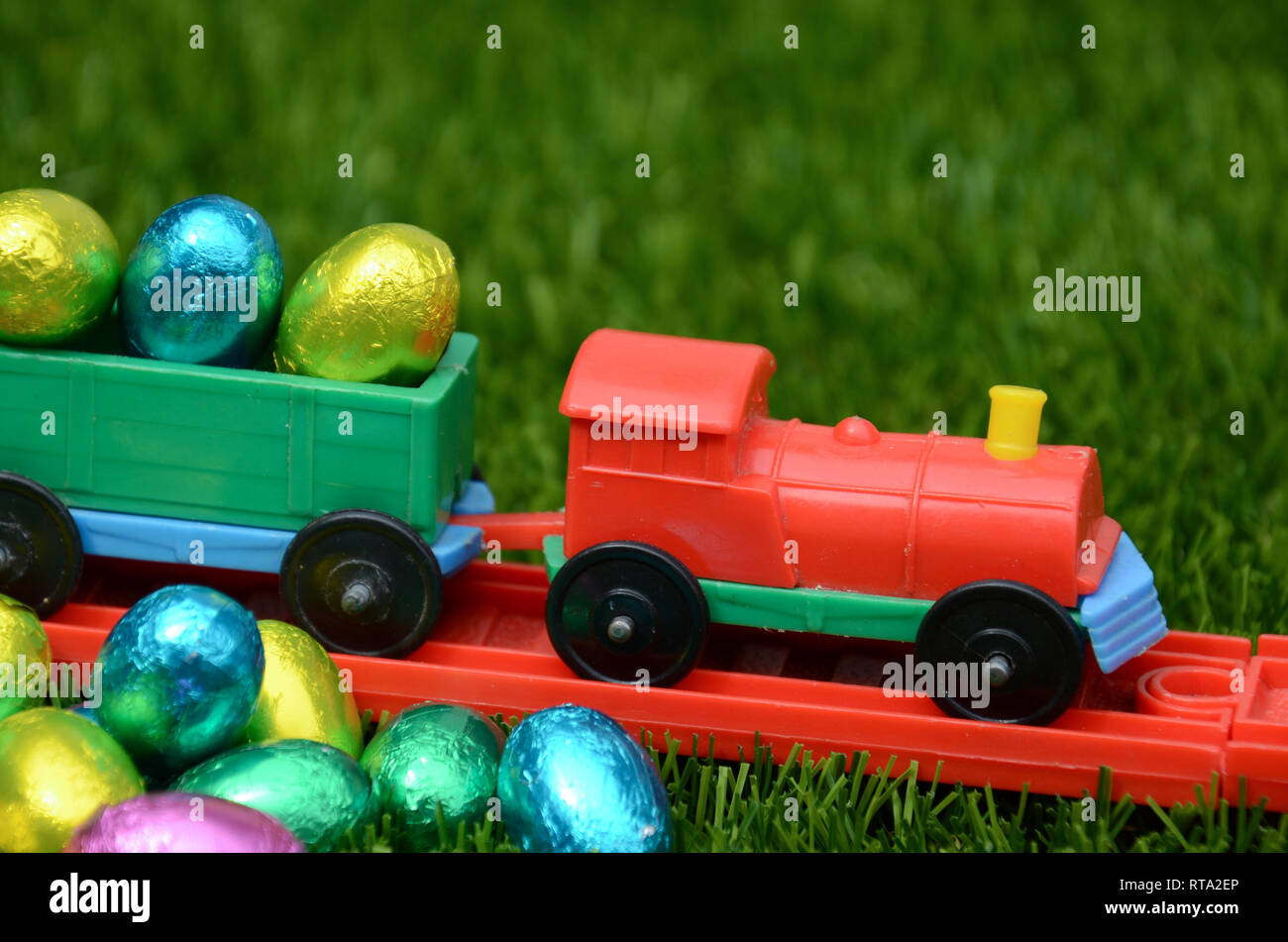 Colorato giocattolo di plastica trasporti treno luminose colorate uova di pasqua sul binario ferroviario sull'erba. Concetto di infanzia, play, i viaggi e le vacanze di pasqua. Foto Stock