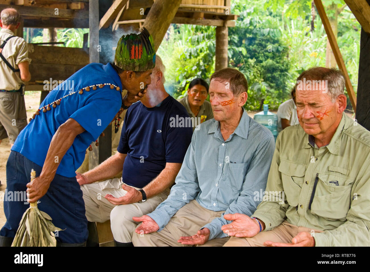 Sciamano soffiando il fumo intorno all uomo; pulizia cerimonia; 3 uomini a occhi chiusi, vernice per il viso, rilassante, Amazzonia Foresta pluviale tropicale; Ecuador; Orizzontale; signor Foto Stock