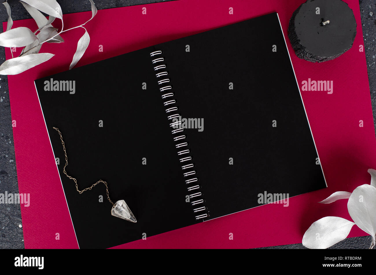 Magic pendolo, nero candela e aperto il notebook con fogli nero su sfondo scuro. Vista dall'alto. Lay piatto Foto Stock