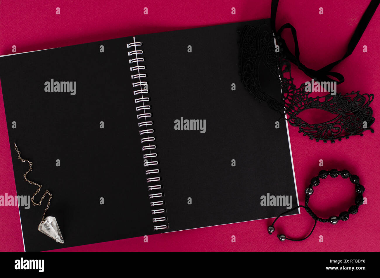 Magic pendolo, maschera nera e aperto il notebook con fogli nero su sfondo scuro. Vista dall'alto. Lay piatto Foto Stock