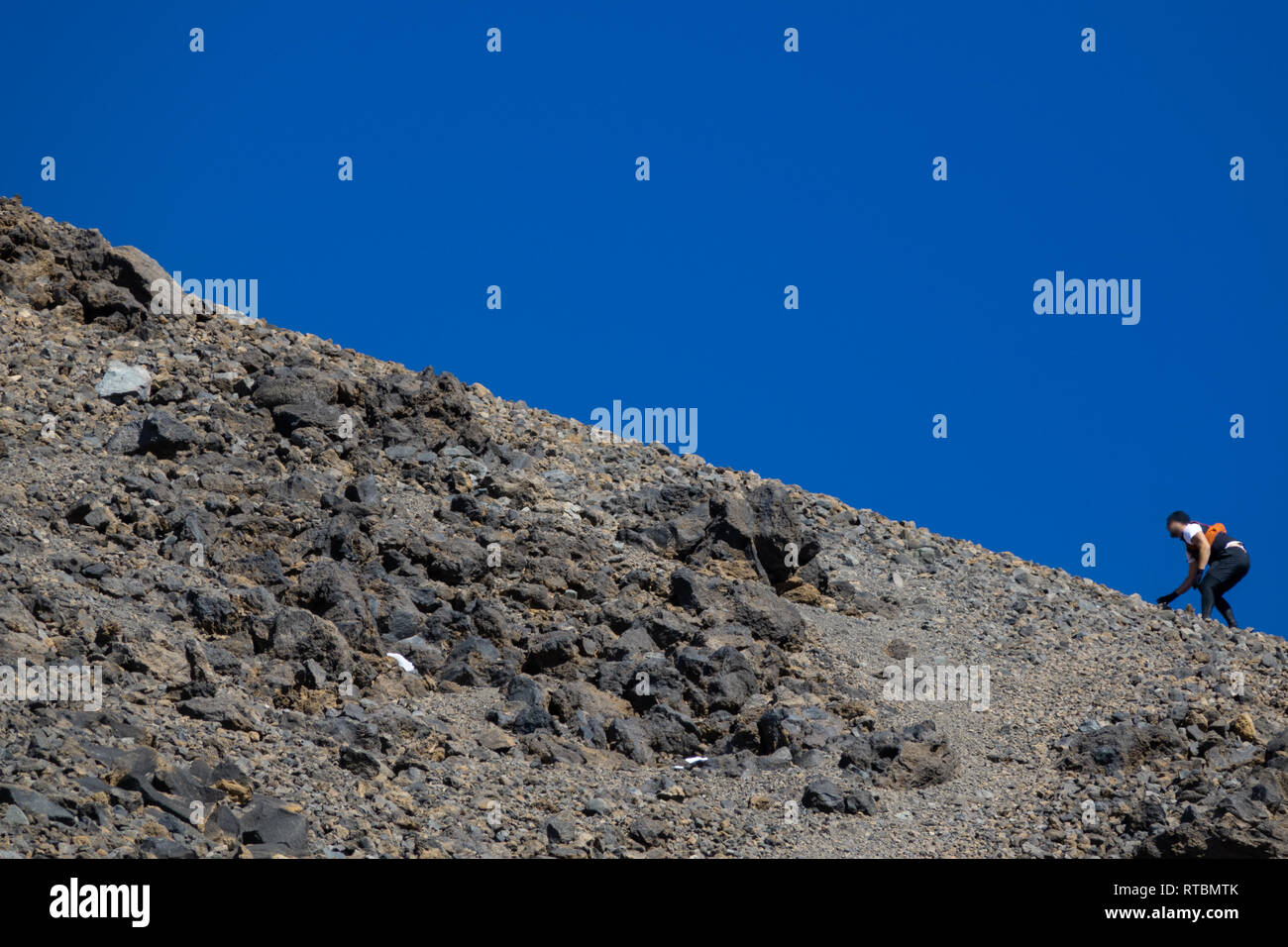 Runner sfocata arrampicata pendio difficile contro il cielo blu Foto Stock