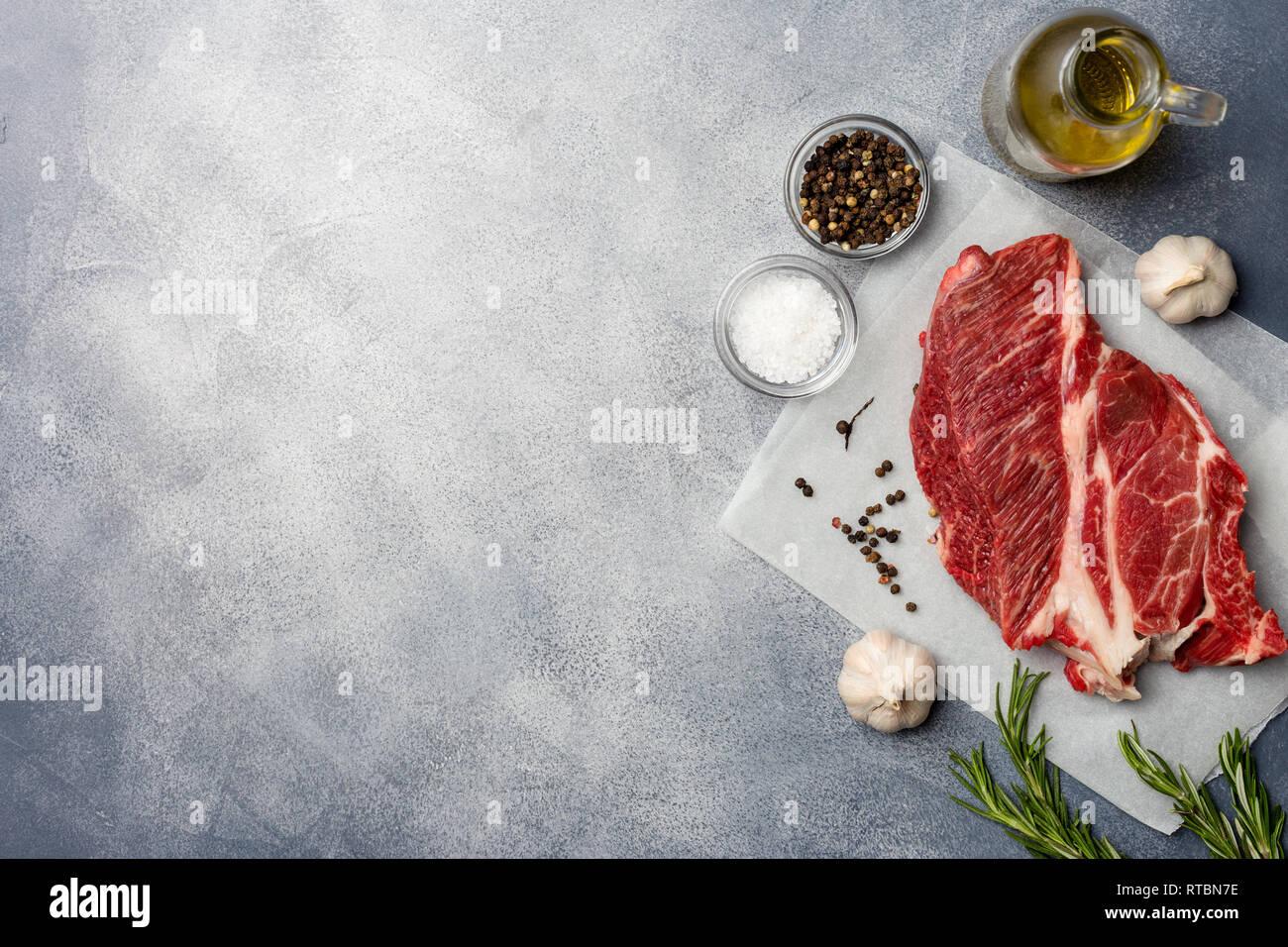 La carne cruda. Materie bistecca con rosmarino, pepe, aglio, olio di oliva e sale. Vista dall'alto. il bordo di destra, copia dello spazio. Foto Stock