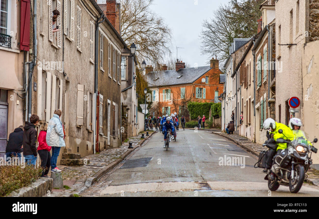 Dampierre-en-Yvelines, Francia - 4 Marzo 2018: il peloton aproaching su una piccola strada tradizionale in un villaggio francese durante Parigi-nizza 2018. Foto Stock
