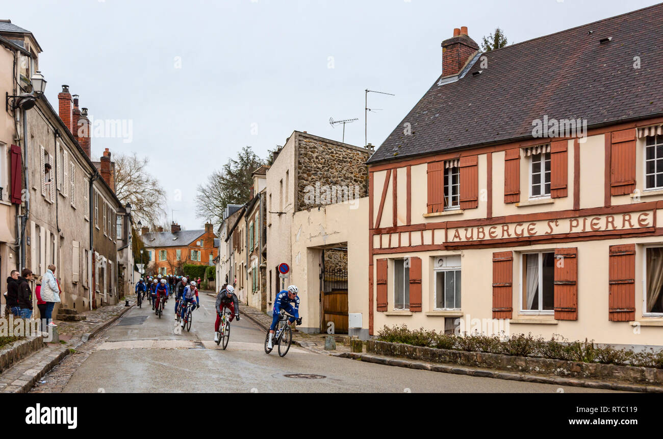 Dampierre-en-Yvelines, Francia - 4 Marzo 2018: il peloton aproaching su una piccola strada tradizionale in un villaggio francese durante Parigi-nizza 2018. Foto Stock