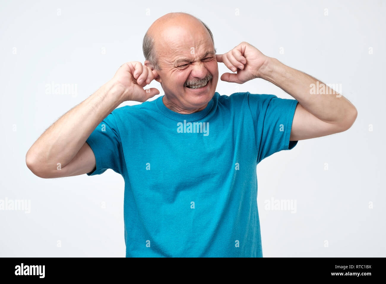 Senior ispanico bald guy collegando le orecchie con le dita sentire suoni ad alto volume della musica pesante da appartamento sopra Foto Stock