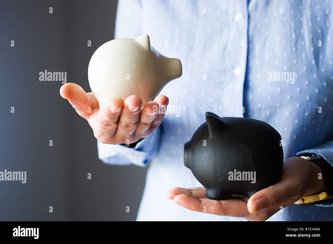 Persona detiene due piggy banche, il bianco è più piccolo e leggero, nero è più grande e più pesante, come il risparmio di debito vs Foto Stock