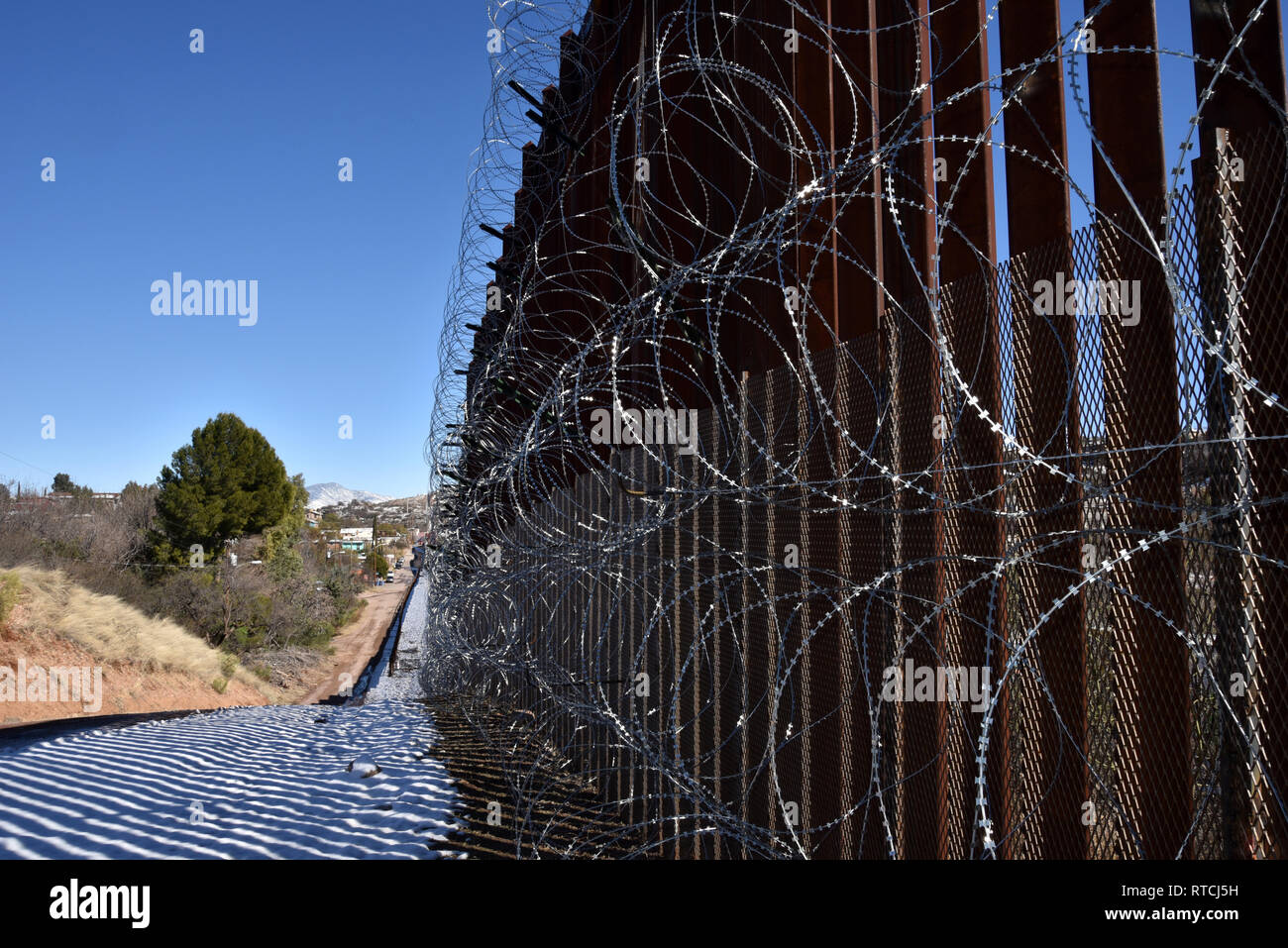 Quattro righe di filo di concertina coprire la parete metallica a Nogales, in Arizona, Stati Uniti d'America, al confine internazionale con Nogales, Sonora, Messico. Foto Stock