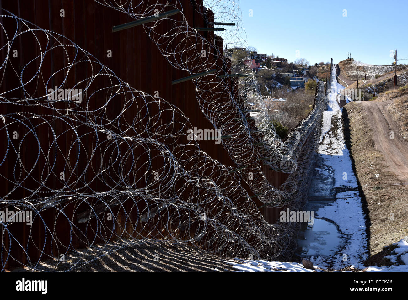 Quattro righe di filo di concertina coprire la parete metallica a Nogales, in Arizona, Stati Uniti d'America, al confine internazionale con Nogales, Sonora, Messico. Foto Stock