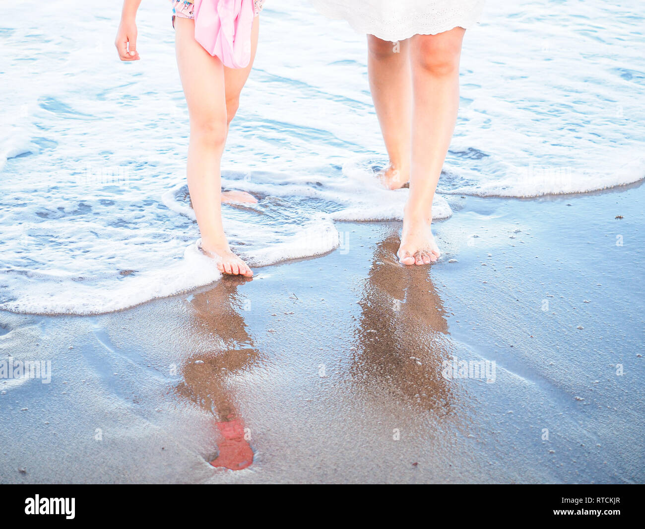Madre e figlia a piedi spuming in acqua di mare schiuma su una spiaggia Foto Stock