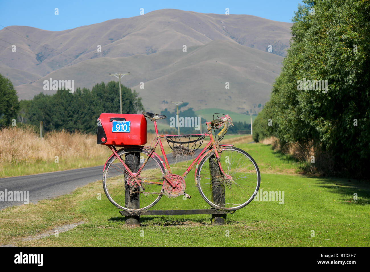 Un rosso letterbox mailbox collegata ad un racing road bike sulla strada di un paese rurale nell'Isola Sud della Nuova Zelanda Foto Stock