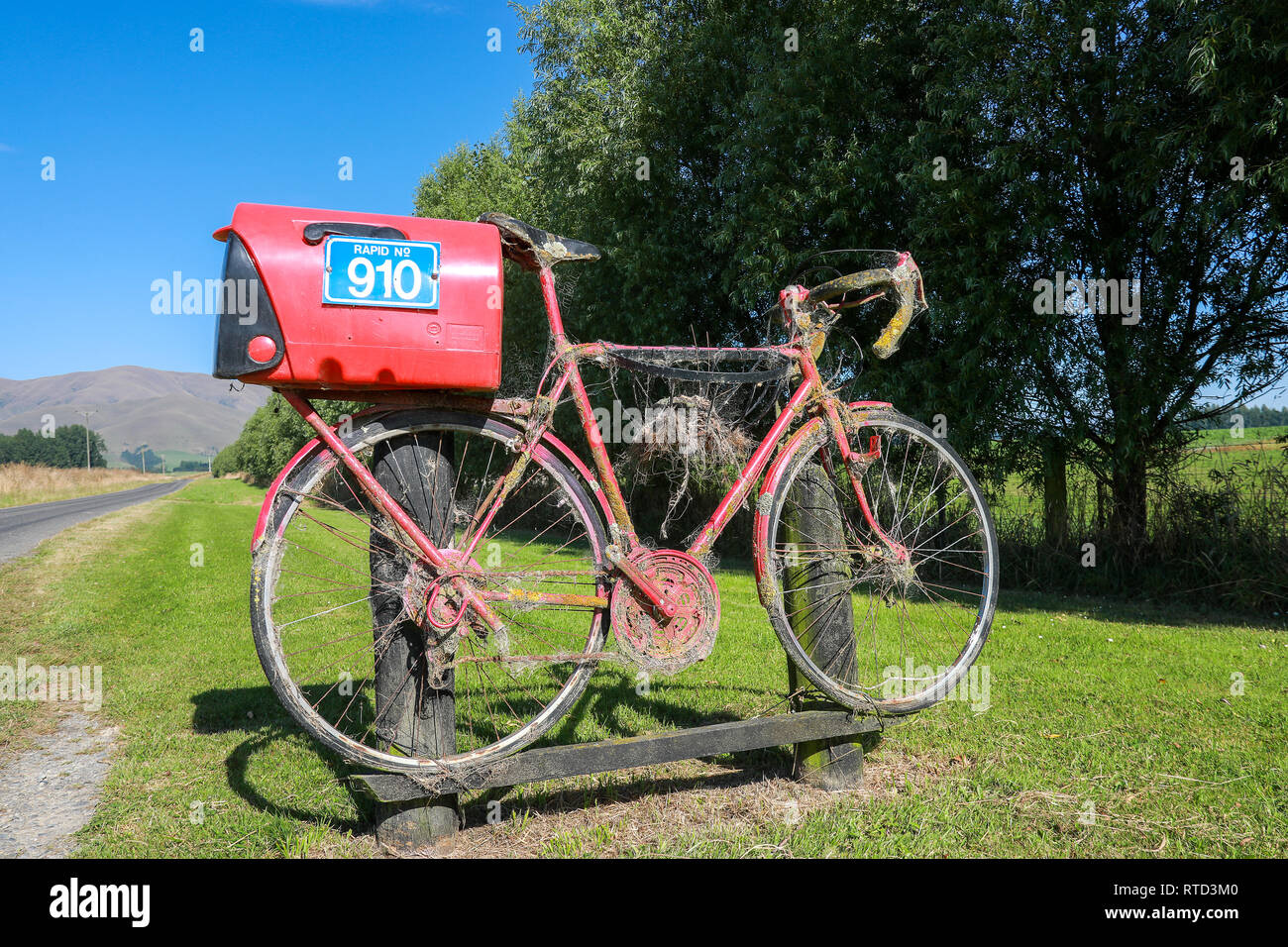 Un rosso letterbox mailbox collegata ad un racing road bike sulla strada di un paese rurale nell'Isola Sud della Nuova Zelanda Foto Stock