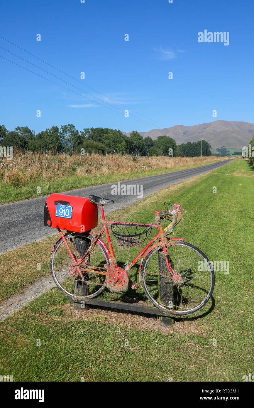 Un rosso letterbox mailbox collegata ad un racing road bike sulla strada di un paese rurale nell'Isola Sud della Nuova Zelanda Foto Stock