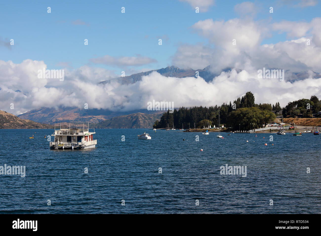 Casa galleggiante su una soleggiata giornata estiva su un calmo lago Wanaka, con montagne Wanaka Wharf, Nuova Zelanda Isola del Sud Foto Stock