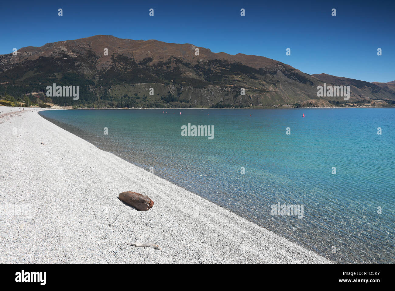 Il bel lago Hawea spiaggia ghiaiosa con driftwood in estate cielo blu acqua chiara ciottoli Rocks'Isola Sud della Nuova Zelanda Foto Stock