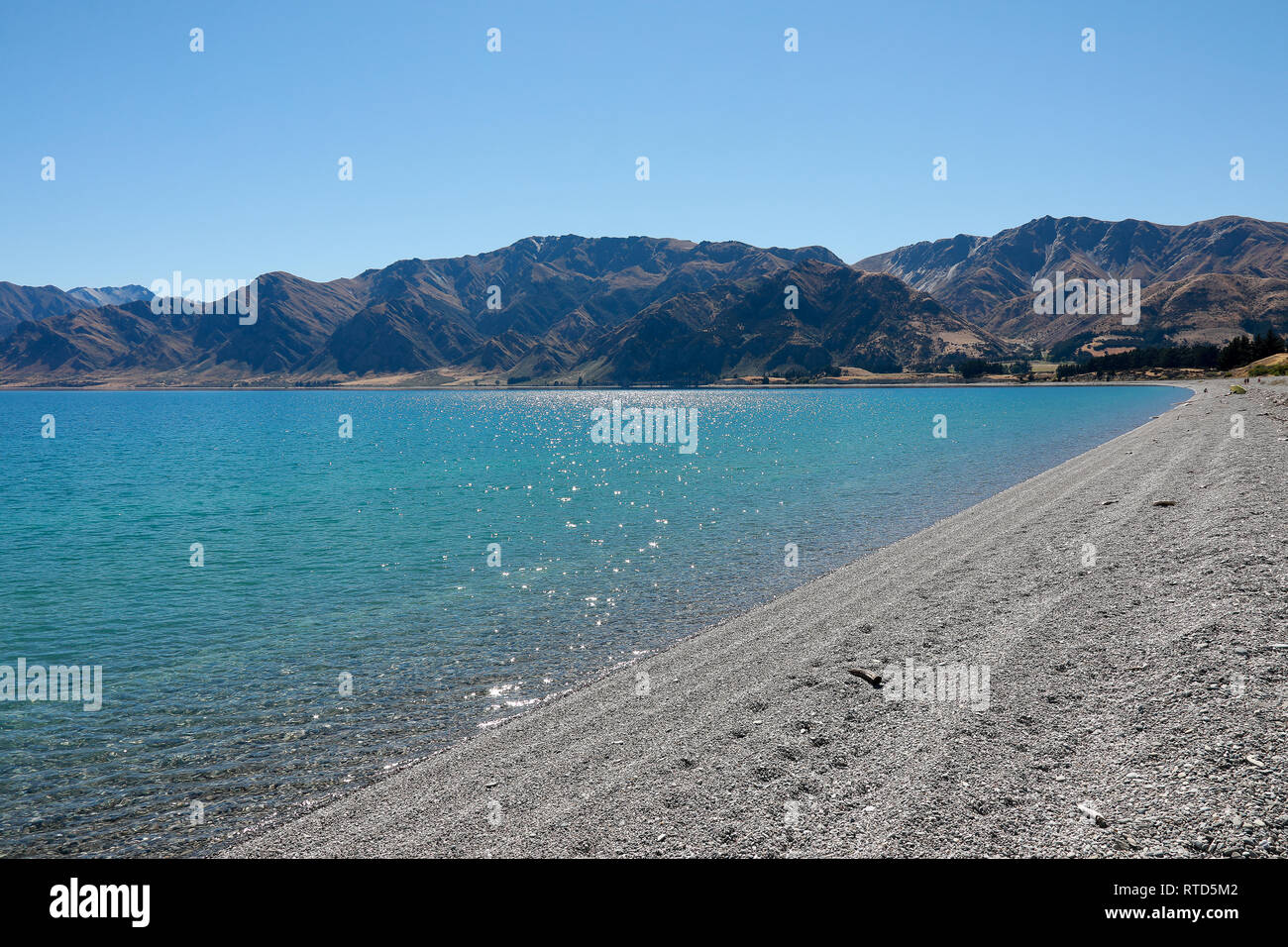 Il bel lago Hawea spiaggia ghiaiosa con driftwood in estate cielo blu acqua chiara ciottoli Rocks'Isola Sud della Nuova Zelanda Foto Stock