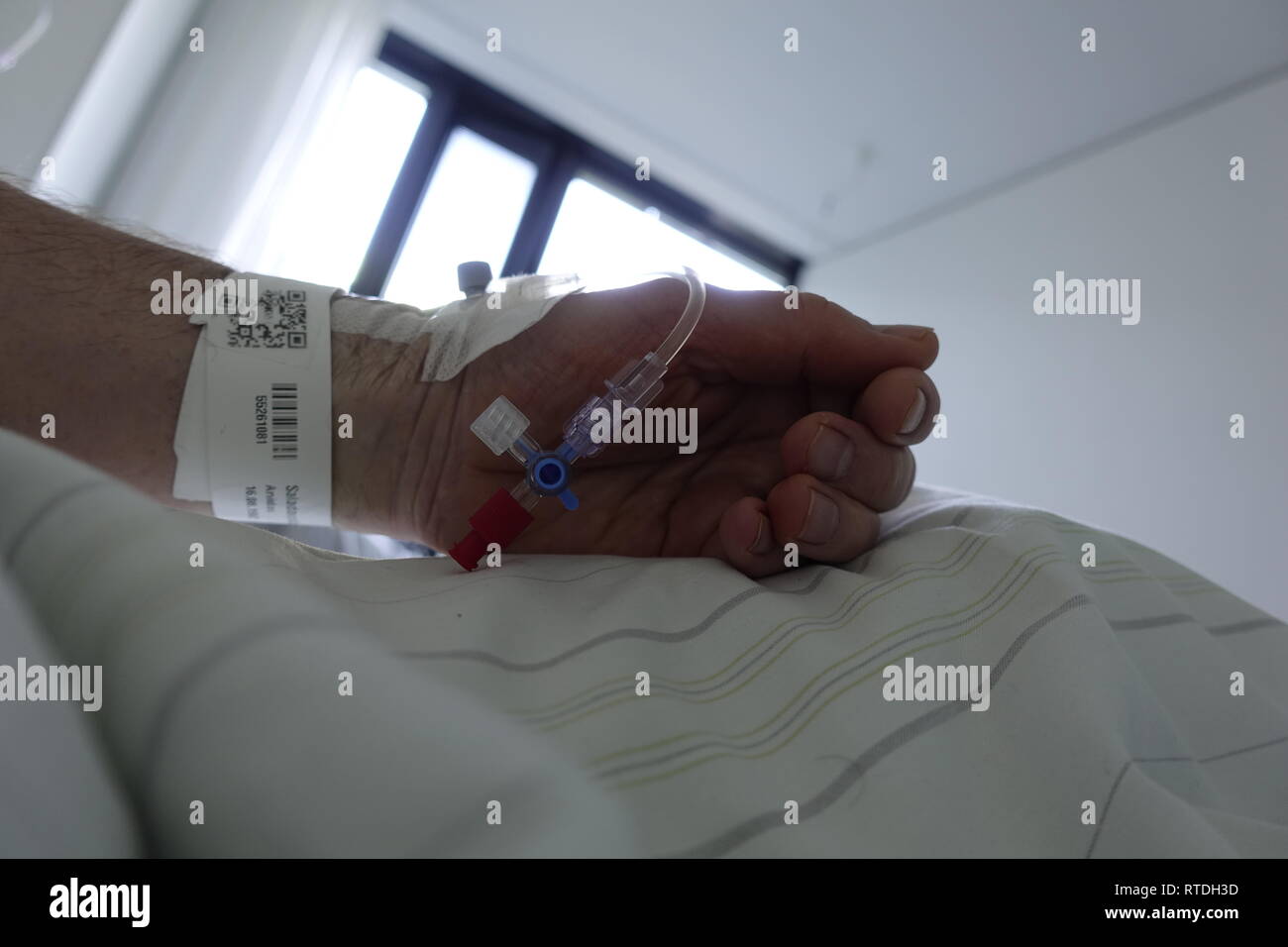 Uomo che indossa un abito ospedale con un IV di linea e di catetere inserito di sua mano. Foto Stock