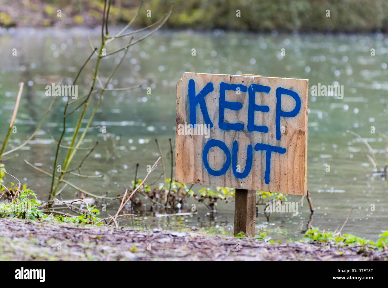 Tenere fuori firma scritta a mano su un cartello in legno infissa a terra da un lago. Foto Stock