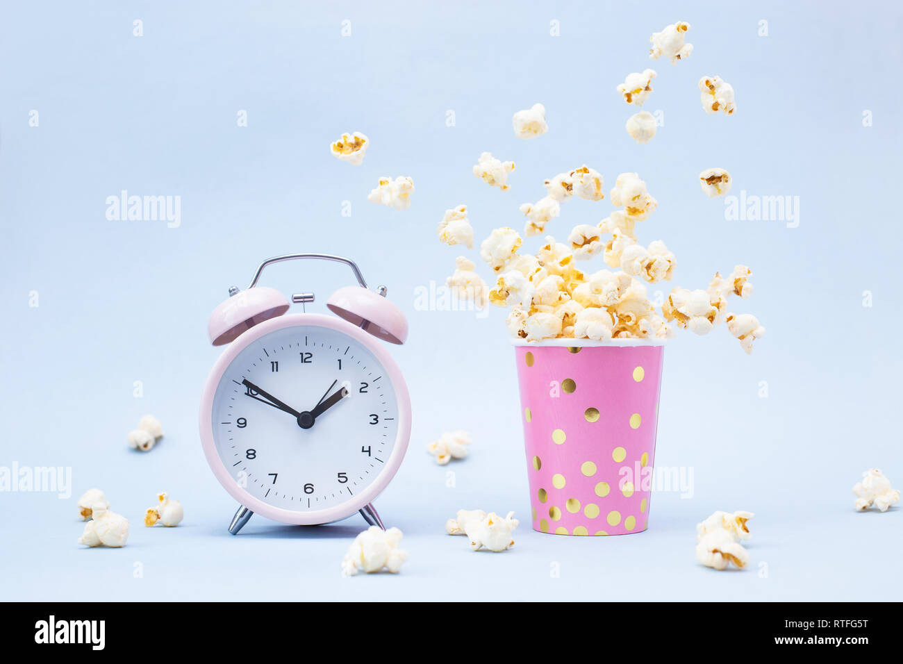 Flying Popcorn in un vetro luminoso e sveglia su uno sfondo blu. Tempo per un concetto di divertimento. Foto Stock