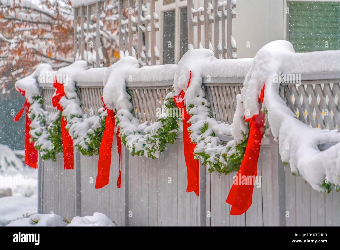 Recinto con ghirlanda nevoso e centine rosso in Alba. White staccionata in legno decorato con una ghirlanda nevoso e rosso vivo archi a dicembre. Frosty scenario Foto Stock