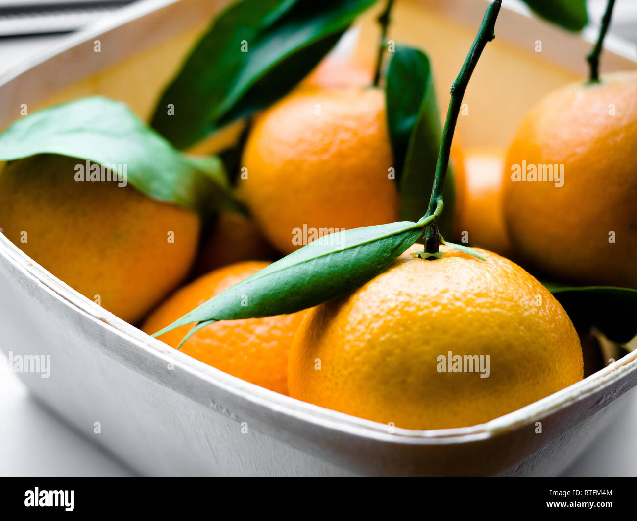 Alcune arance con foglie in un cestello, Arancione Tangerini in un cesto su uno sfondo bianco. Foto Stock