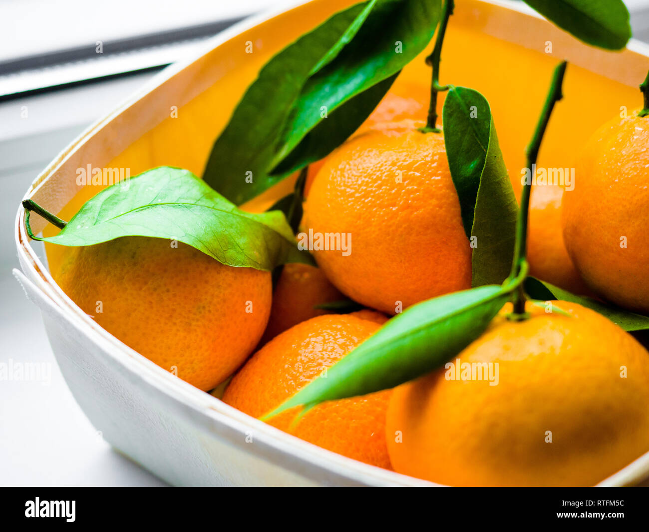 Alcune arance con foglie in un cestello, Arancione Tangerini in un cesto su uno sfondo bianco. Foto Stock