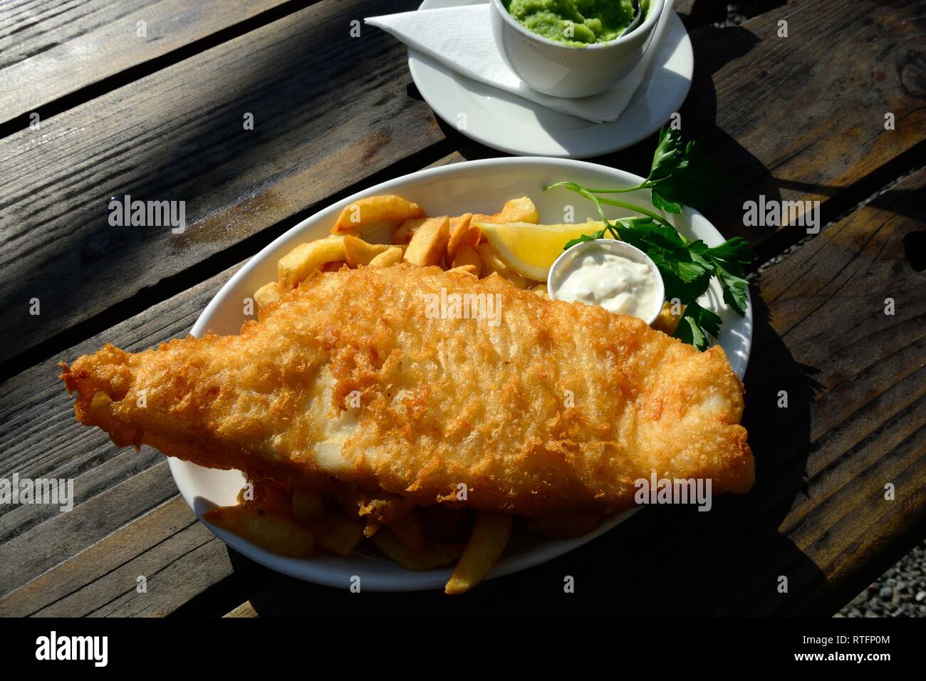 Pesce e patatine con fiacco piselli su un tavolo all'esterno del capannone Bistro Porthgain Pembrokeshire Wales Cymru REGNO UNITO GB Foto Stock