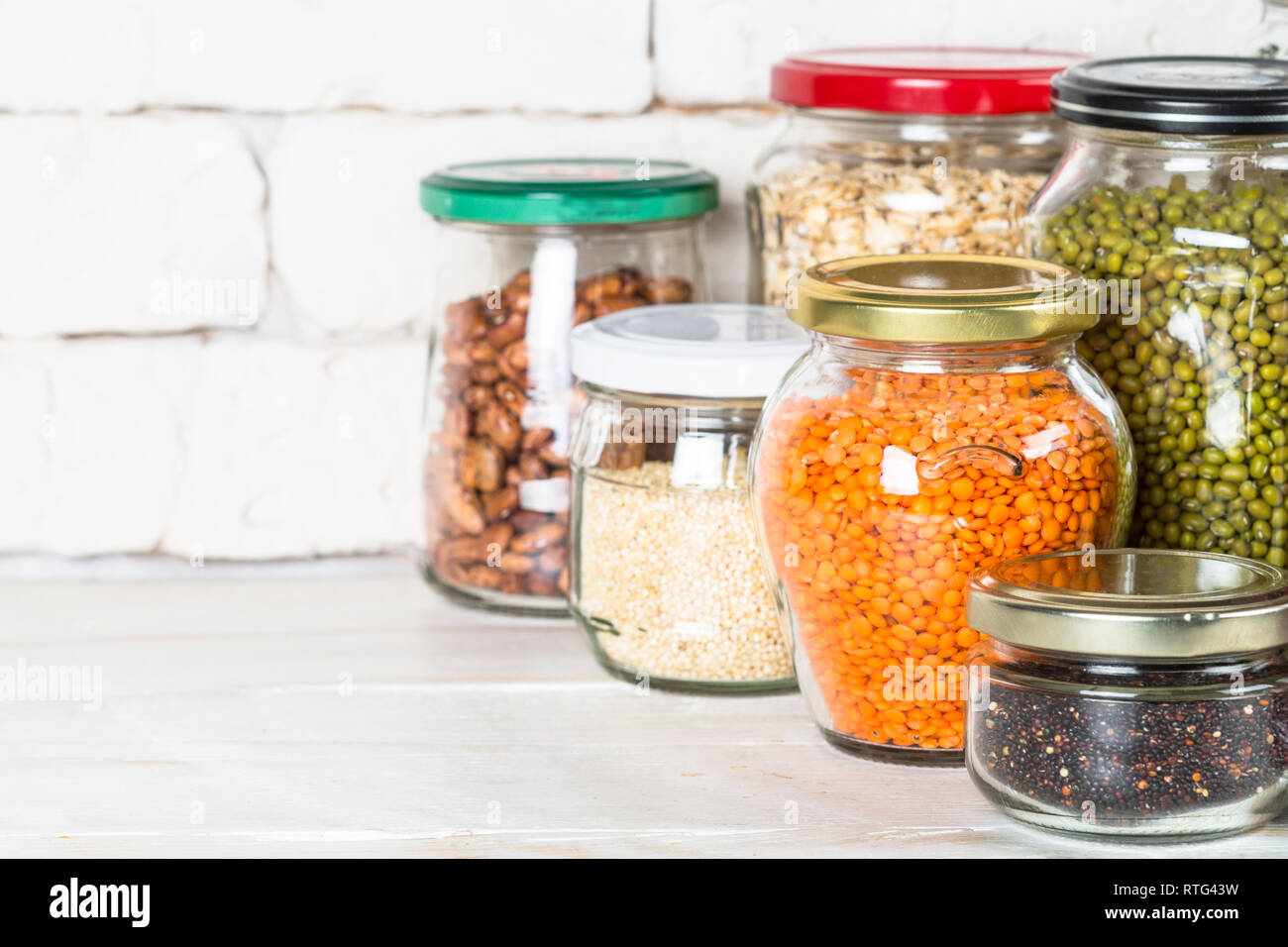 Cereali, legumi e fagioli in barattoli di vetro bianco sul tavolo da cucina. Foto Stock