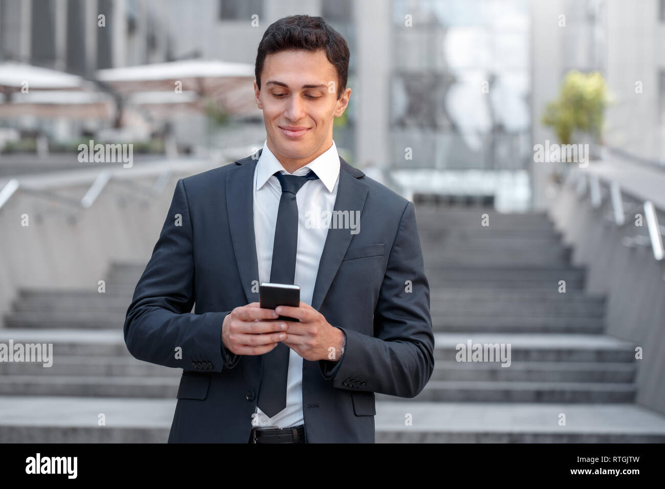 Young business man standing sulla strada di città il controllo sociale dei media sullo smartphone durante il tempo libero a sorridere gioiosa Foto Stock