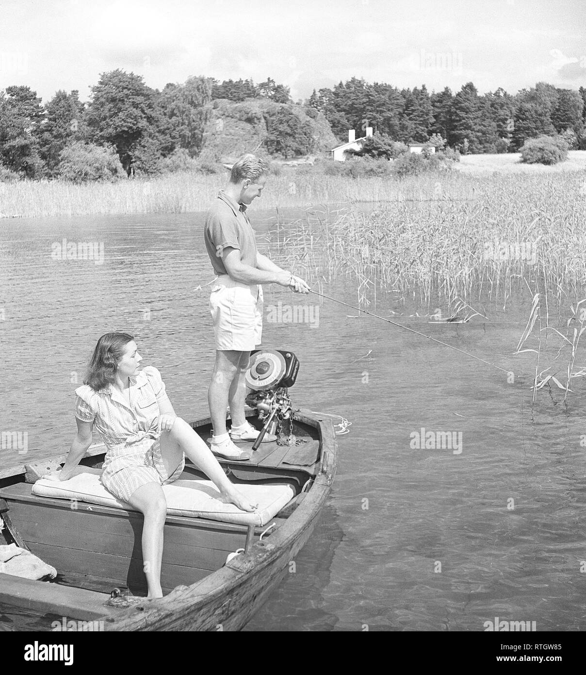 La pesca nel 1940s. Un uomo è la pesca dalla barca e la sua fidanzata è godendo il sole mentre in attesa per lui per catturare un pesce. Il motore fuoribordo viene fatta dal produttore svedese di Penta. In tutto il mondo il nome Penta è diventato sinonimo con motore fuoribordo in molte lingue. Foto Kristoffersson ref AC119-5 Svezia 1946 Foto Stock