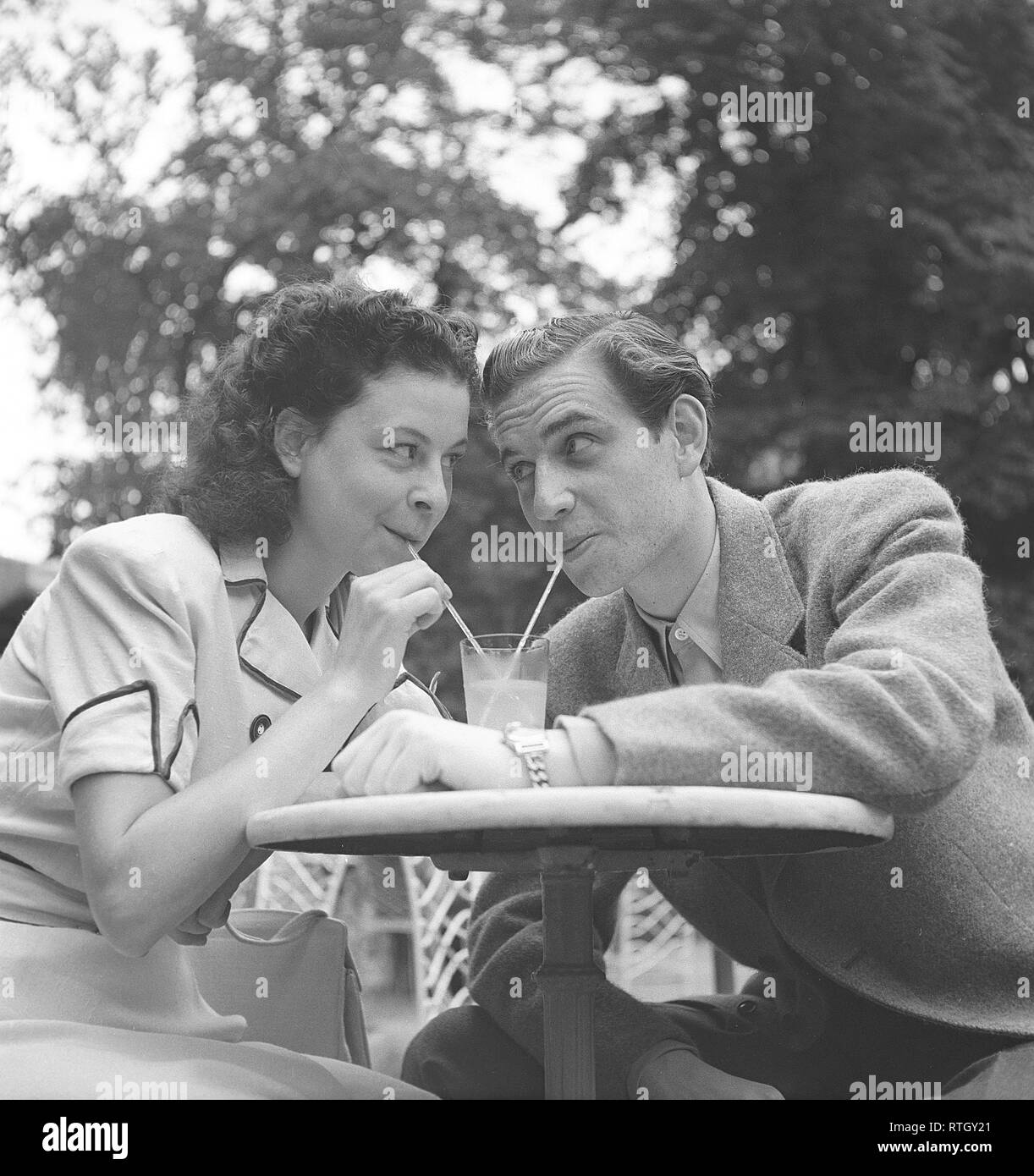 1940s lifestyle. Una giovane coppia in un caffè all'aperto. Essi sono di bere dallo stesso bicchiere di limonata con cannucce. La Svezia. Foto Kristoffersson Ref U89-2. La Svezia 1946 Foto Stock