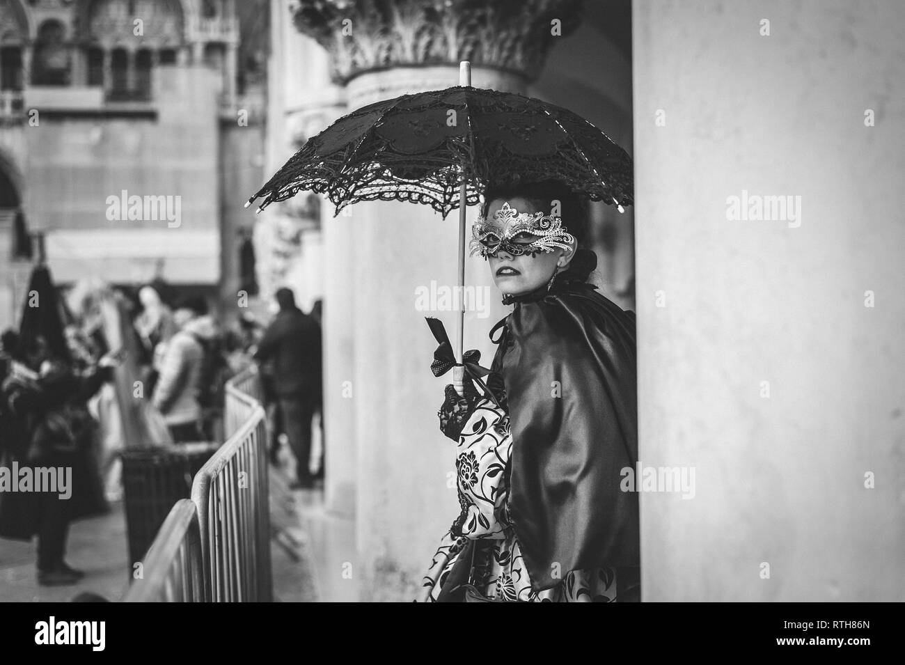 B/W donna mascherata con un ombrello in piedi sotto un arco durante il carnevale di Venezia Foto Stock