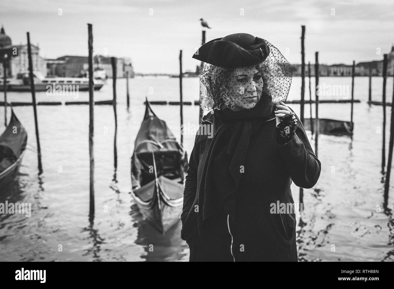 Il carnevale donna mascherata in piedi vicino alla laguna veneziana in un ritratto in bianco e nero image Foto Stock