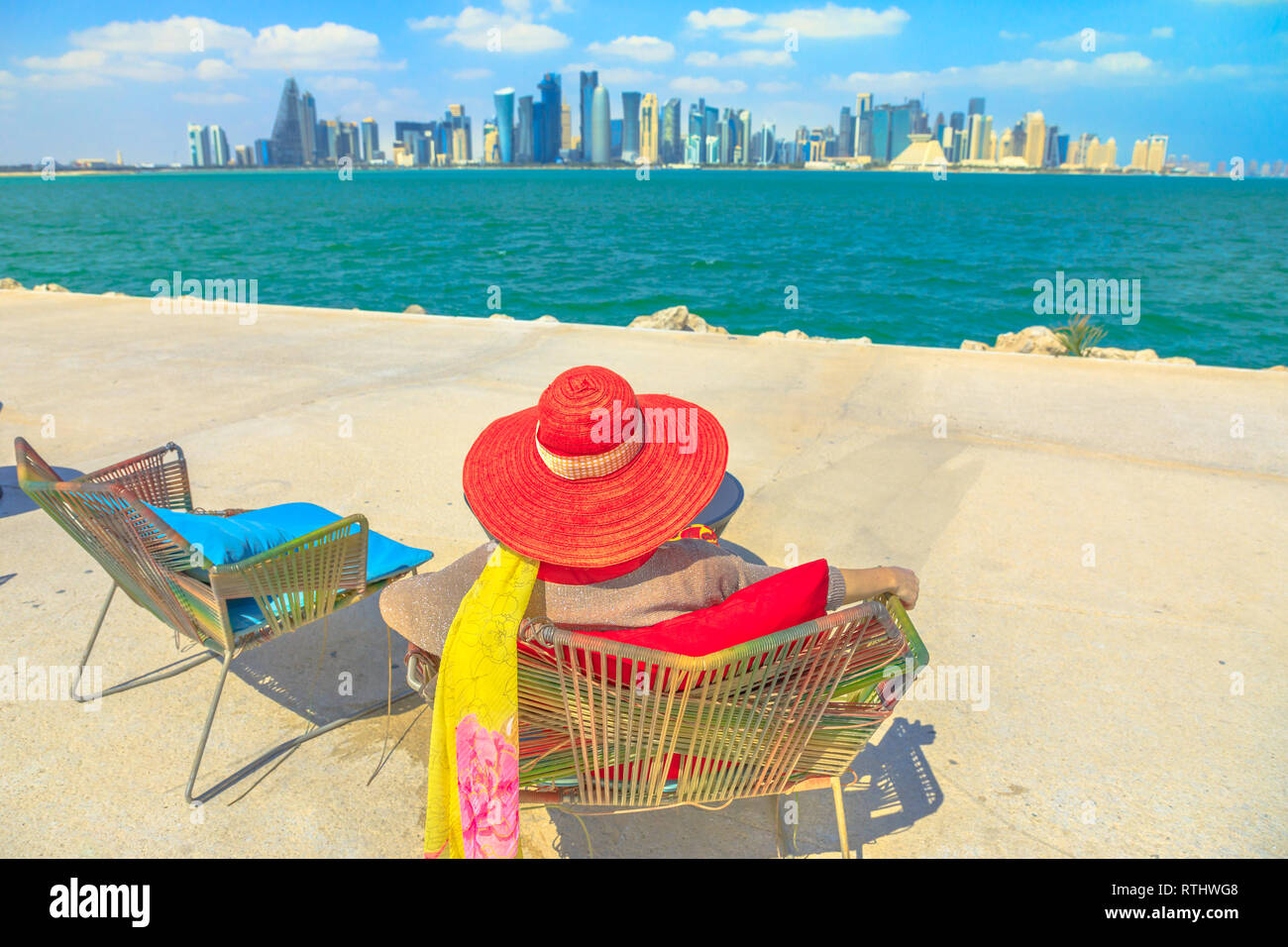 Eleganti donna con cappello cercando la vista della baia di Doha in una giornata di sole. Stile di vita turistica caucasica gode di grattacieli di Doha skyline del centro a Foto Stock