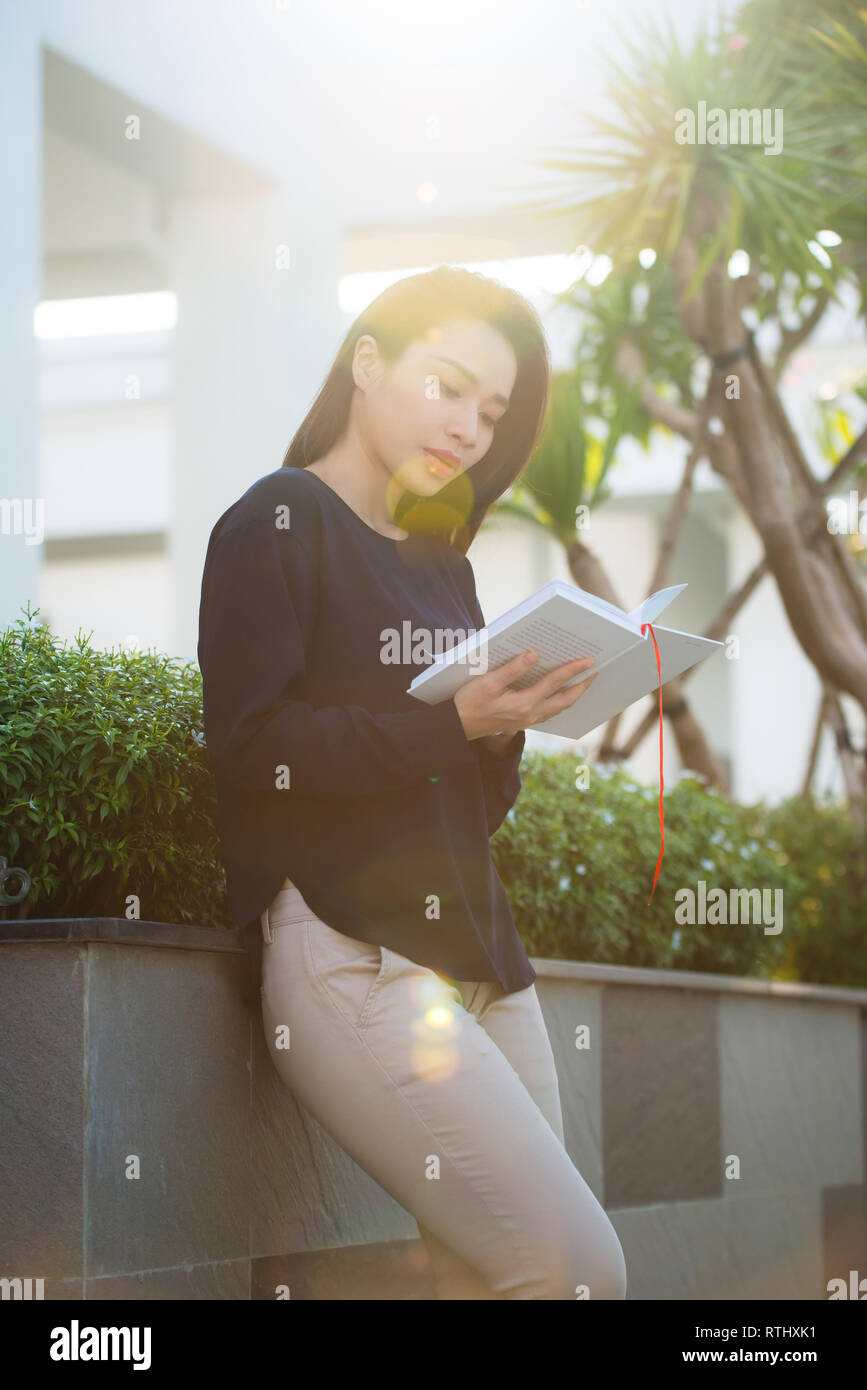 Ritratto di donna sorridente studente libro di lettura permanente, mentre all'aperto sulla terrazza del campus cafe nella giornata di sole. Istruzione, lo stile di vita e il concetto di popolo Foto Stock