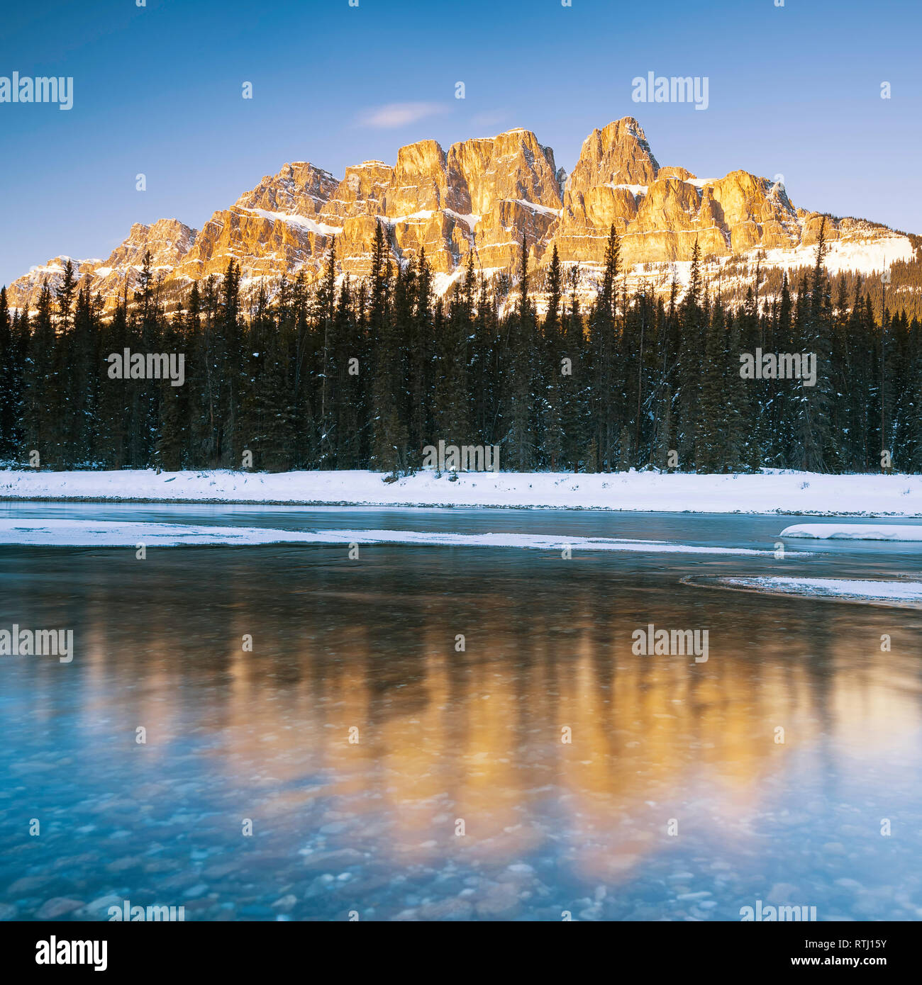 Sunset lunga esposizione del tardo sun afferrando la parte superiore della coperta di neve Castle Mountain e il Fiume Bow nel Parco Nazionale di Banff, Canada Foto Stock