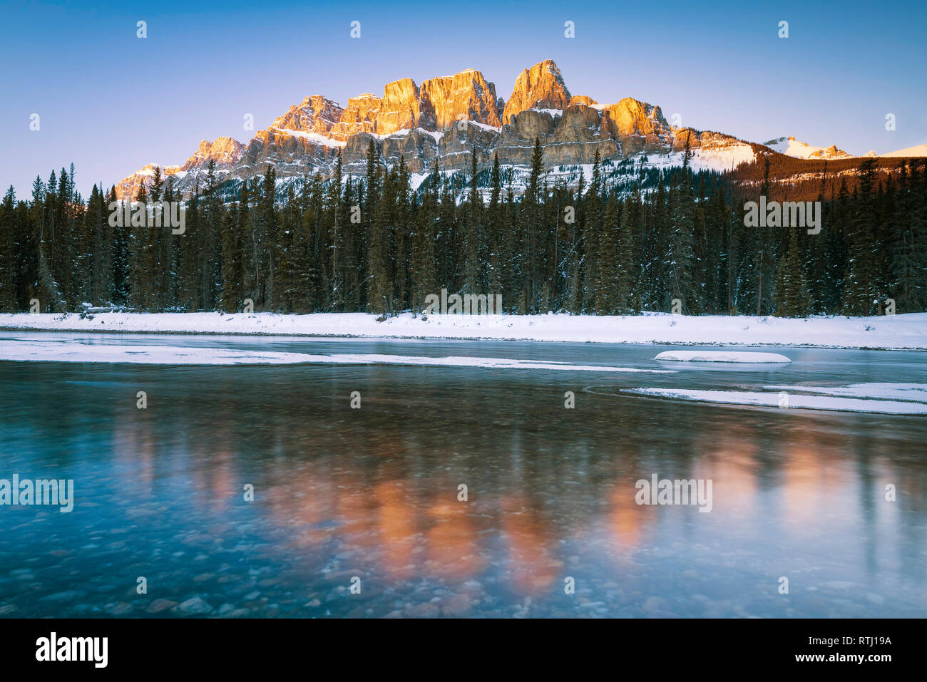 Sunset lunga esposizione del tardo sun afferrando la parte superiore della coperta di neve Castle Mountain e il Fiume Bow nel Parco Nazionale di Banff, Canada Foto Stock