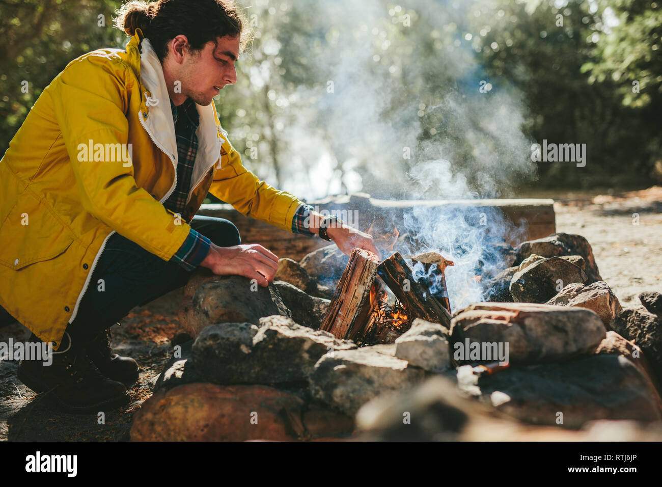 L'uomo la messa fuoco a legna in un falò in una foresta. Uomo in campeggio in una località di campagna impostazione a un falò. Foto Stock