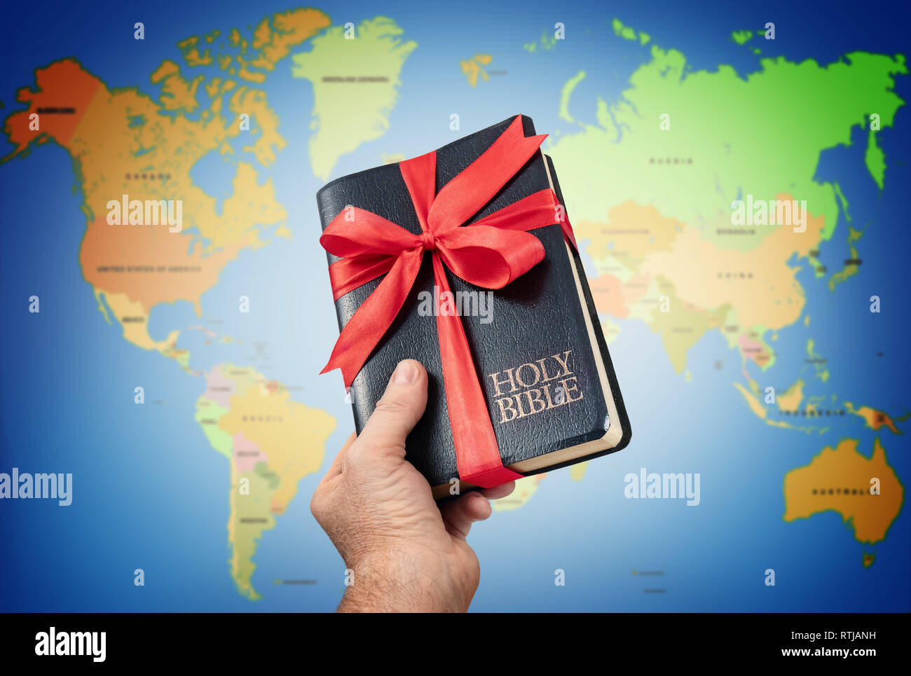 Dando a mano la Sacra Bibbia dono contro la mappa del mondo. Foto Stock
