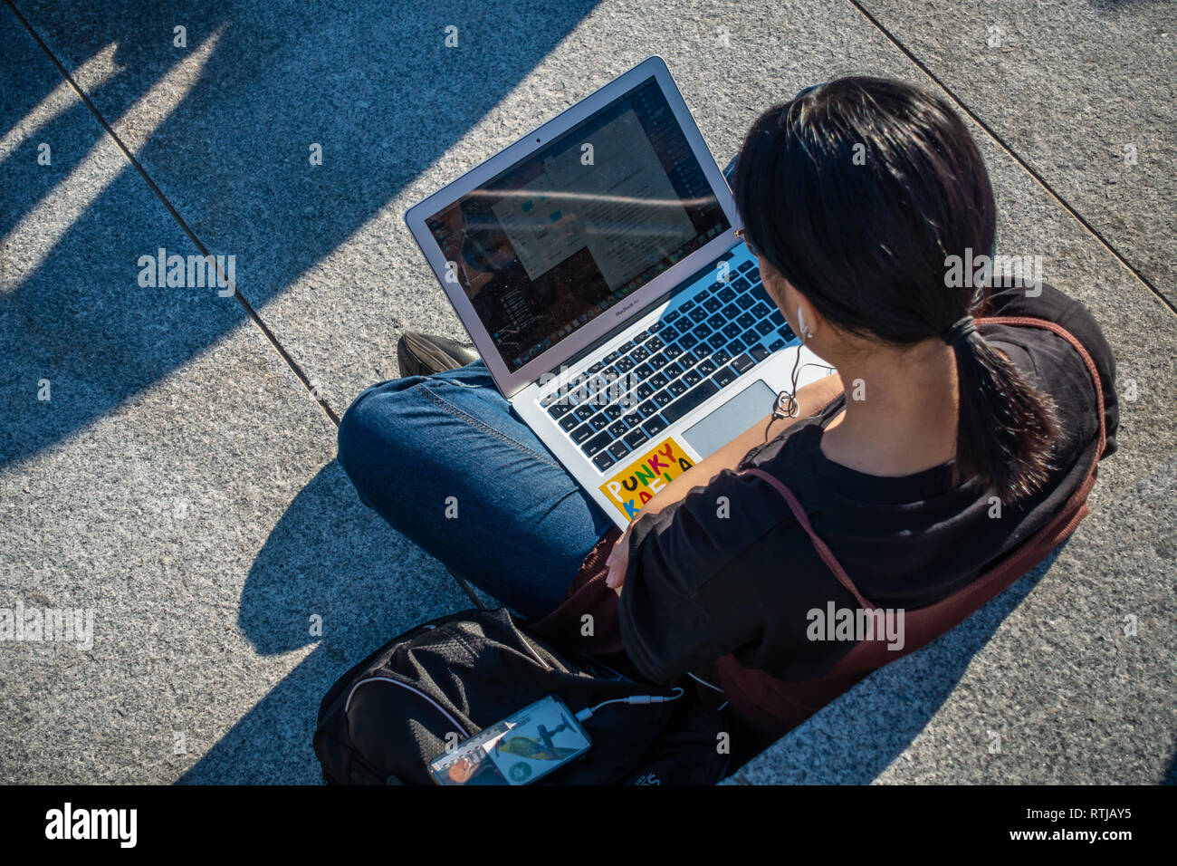Immagine da sopra della giovane donna seduta al di fuori nel sole e utilizzando il suo laptop e telefoni cellulari a gocce di carbone cantiere, Kings Cross a Londra, Inghilterra Foto Stock