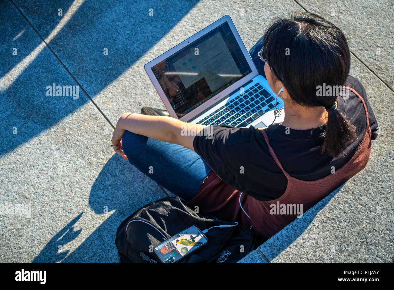 Immagine da sopra della giovane donna seduta al di fuori nel sole e utilizzando il suo laptop e telefoni cellulari a gocce di carbone cantiere, Kings Cross a Londra, Inghilterra Foto Stock