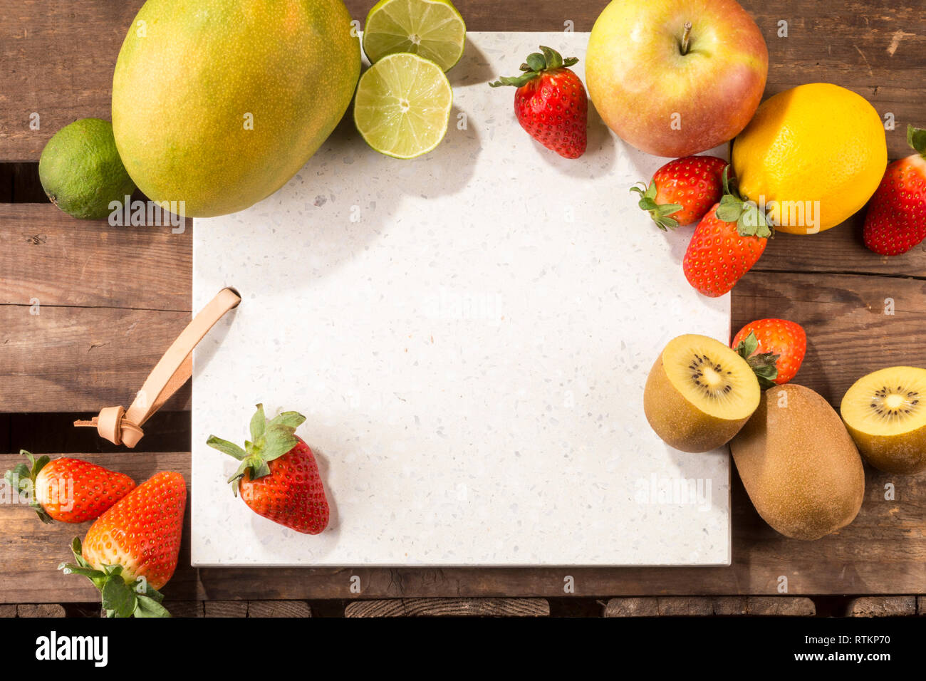 Pietra di calcestruzzo server con spazio per il testo su un legno rustico listone superficie. e disposti frutti. Apple, limone, fragole, kiwi, tigli e mango. Foto Stock