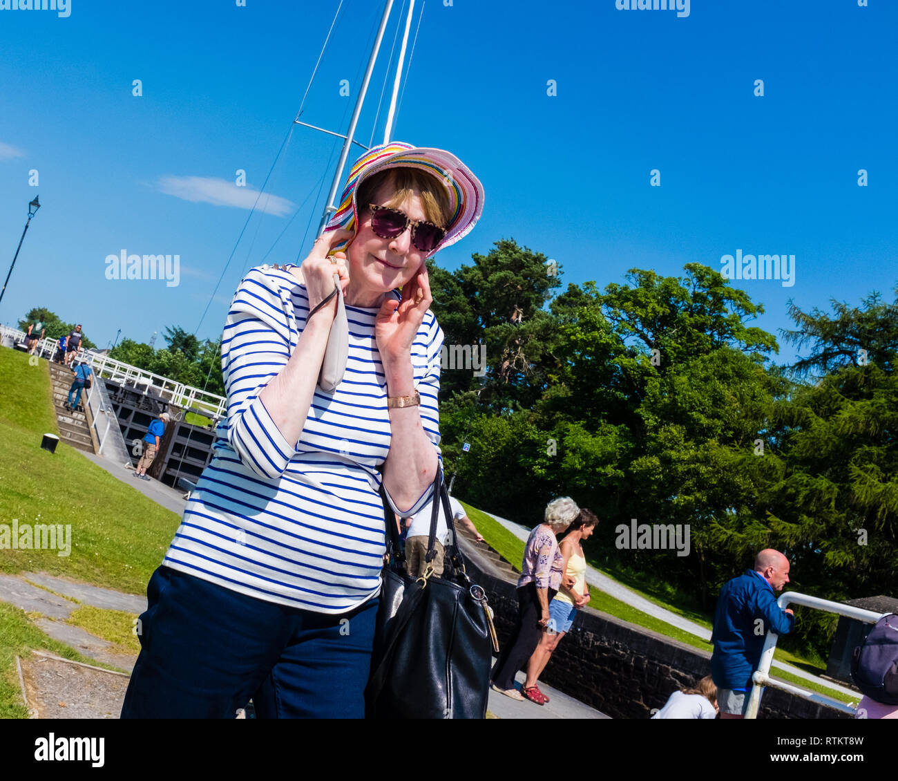 Signora trattenendo il suo cappello da sole nella brezza estiva neptunes scalinata caledonian canal Fort William highlands scozzesi Foto Stock