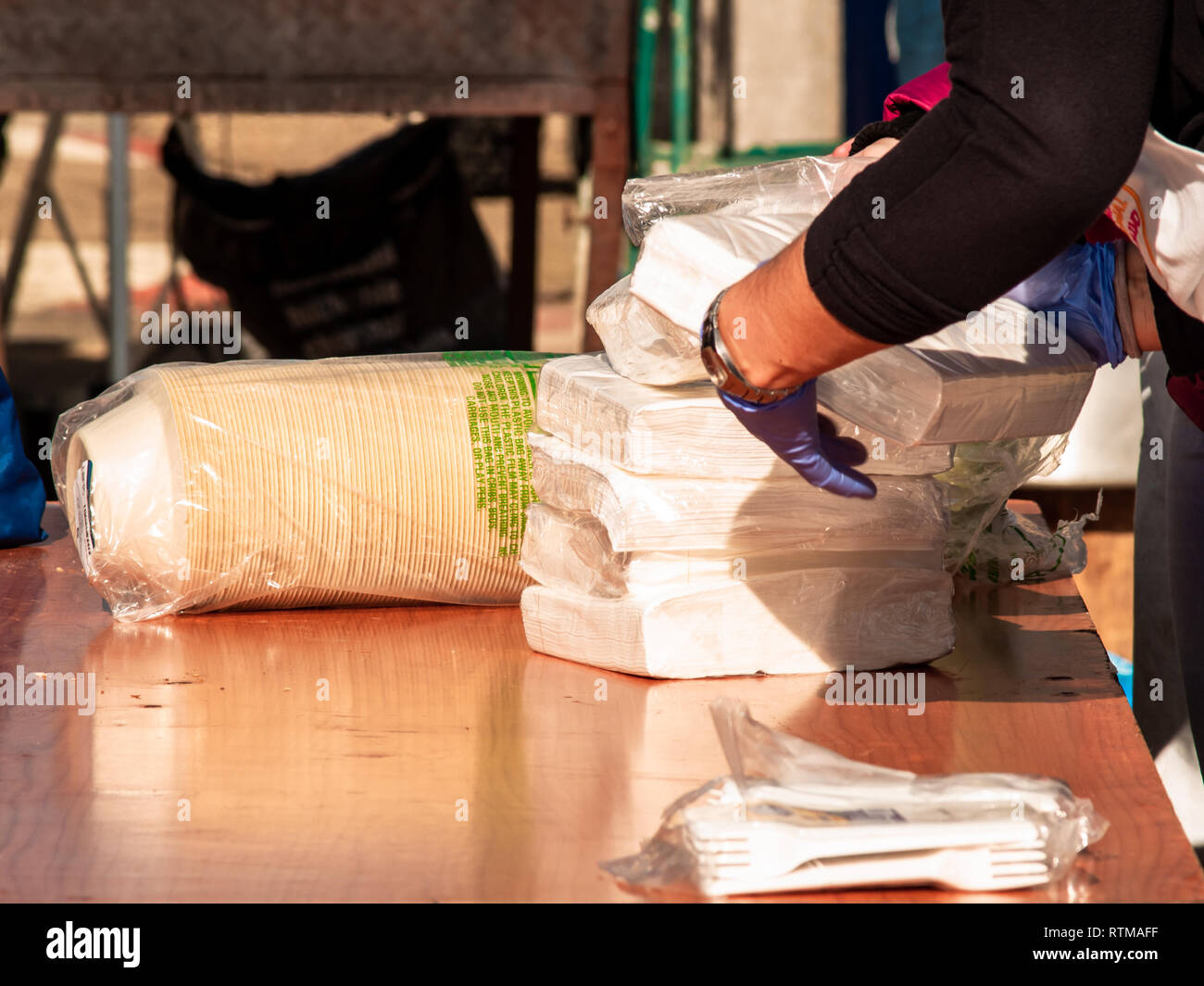 Una persona che indossa guanti in nitrile blu immissione di tovaglioli di carta, plastica forcelle e piastre di carta su un tavolo durante una festa di strada Foto Stock