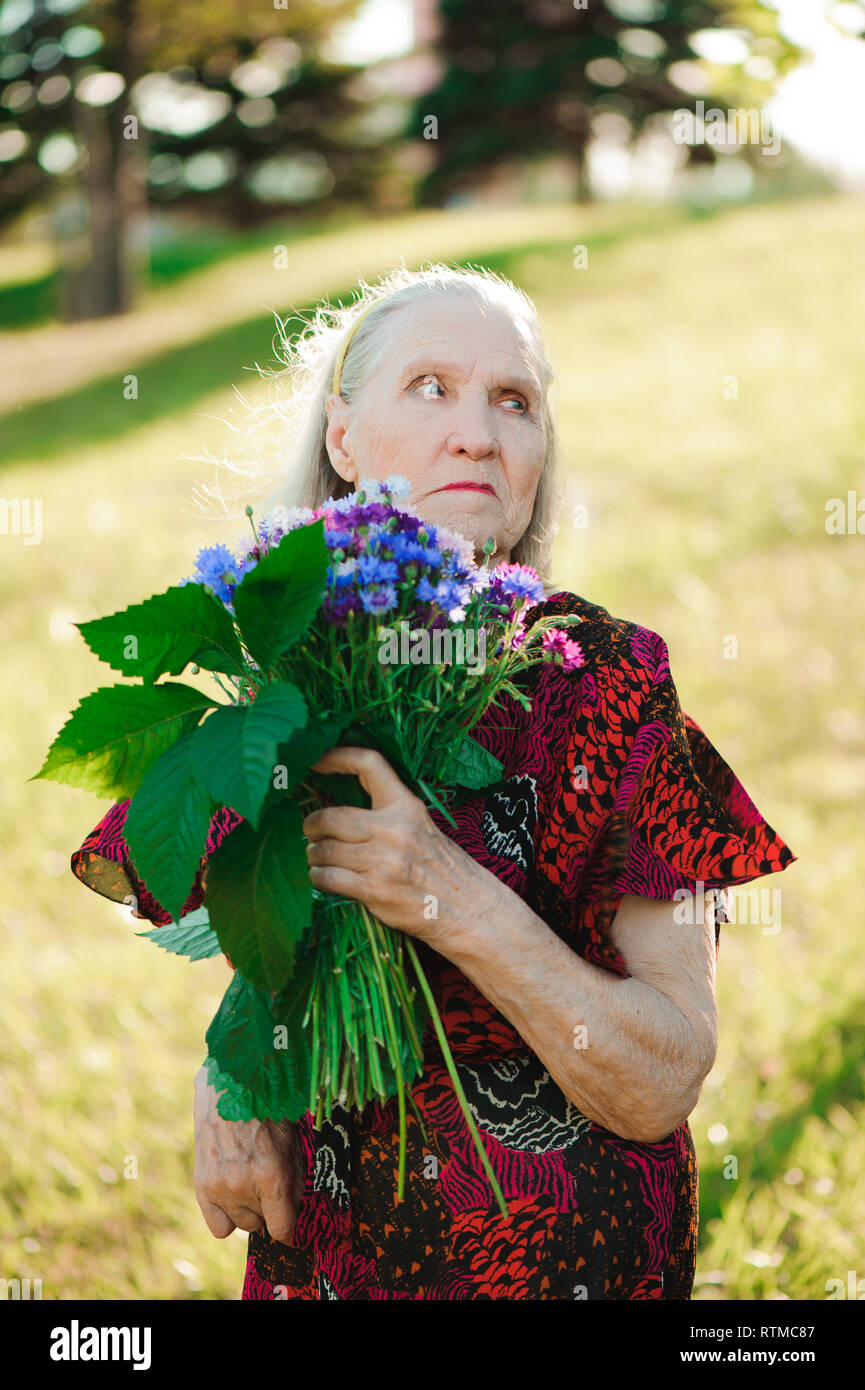 80 anno vecchia donna con un mazzo di fiori nelle sue mani. Foto Stock