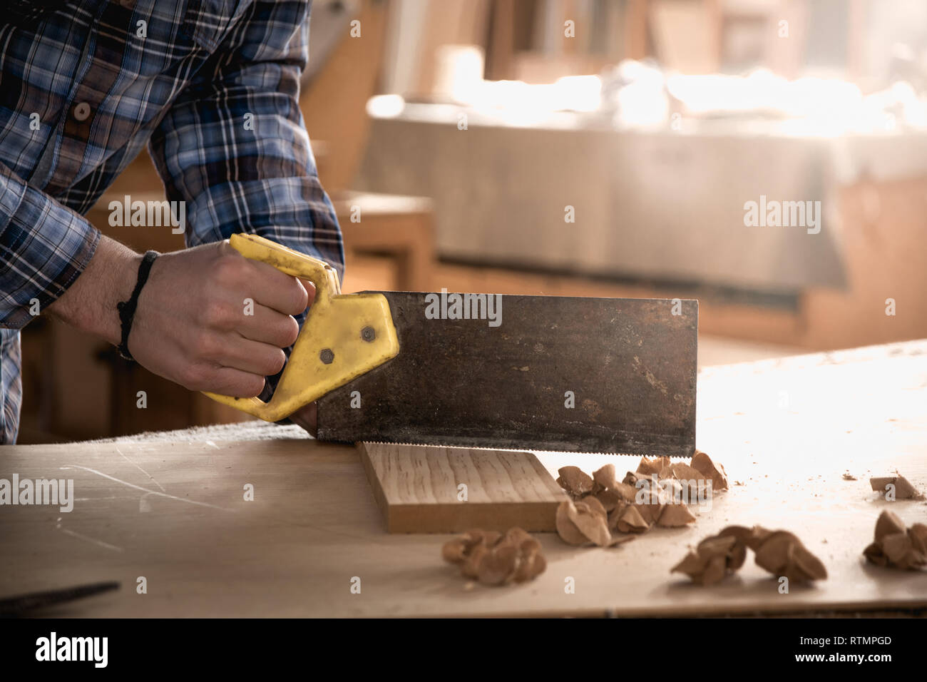 Carpenter lavora con sega sul legno. Workshop sullo sfondo. Carpenter workbench. Foto Stock