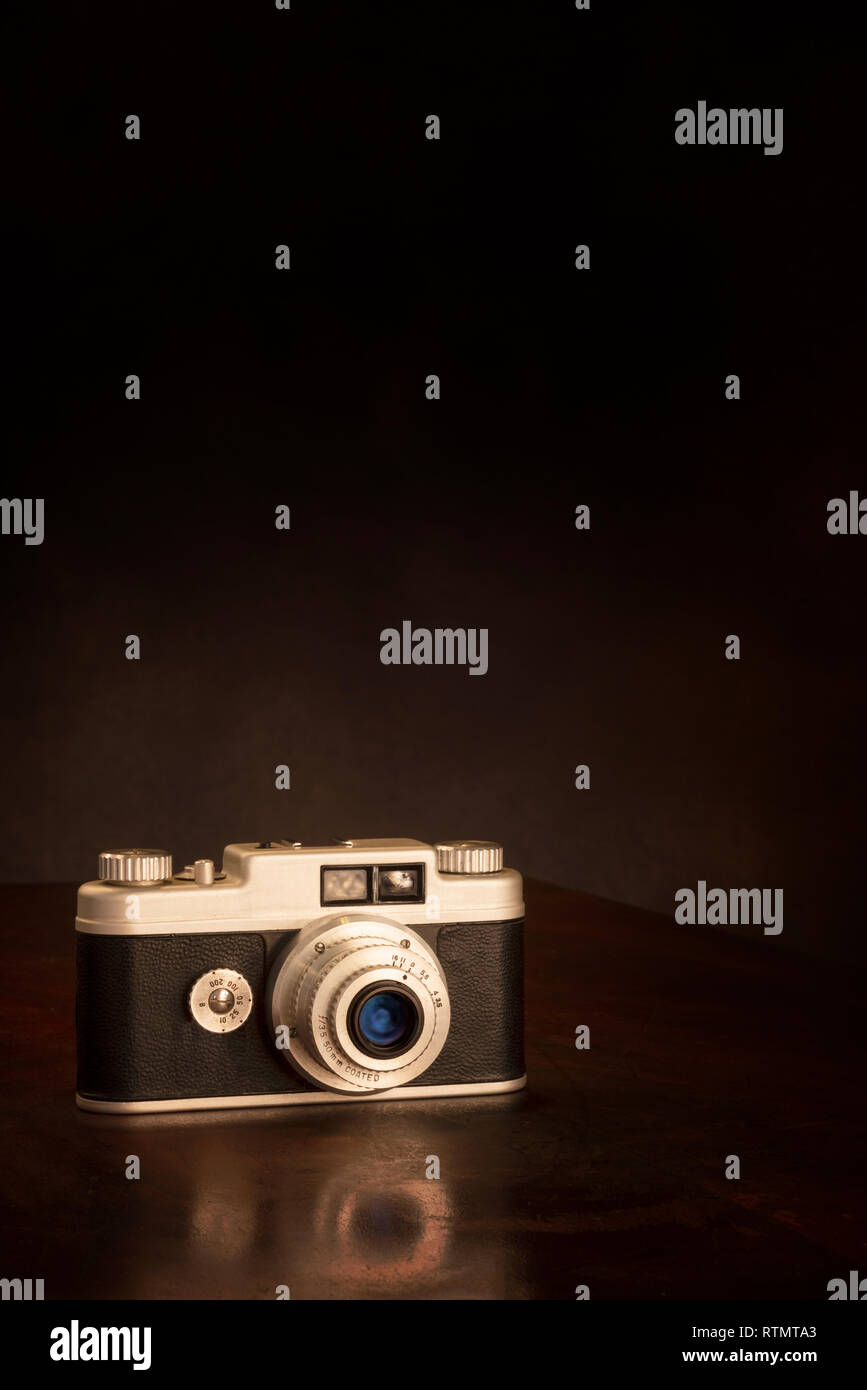Colpo verticale di una vecchia macchina fotografica da 35mm su uno sfondo marrone con copia spazio. La riflessione parziale della telecamera sul piano portapaziente. Foto Stock